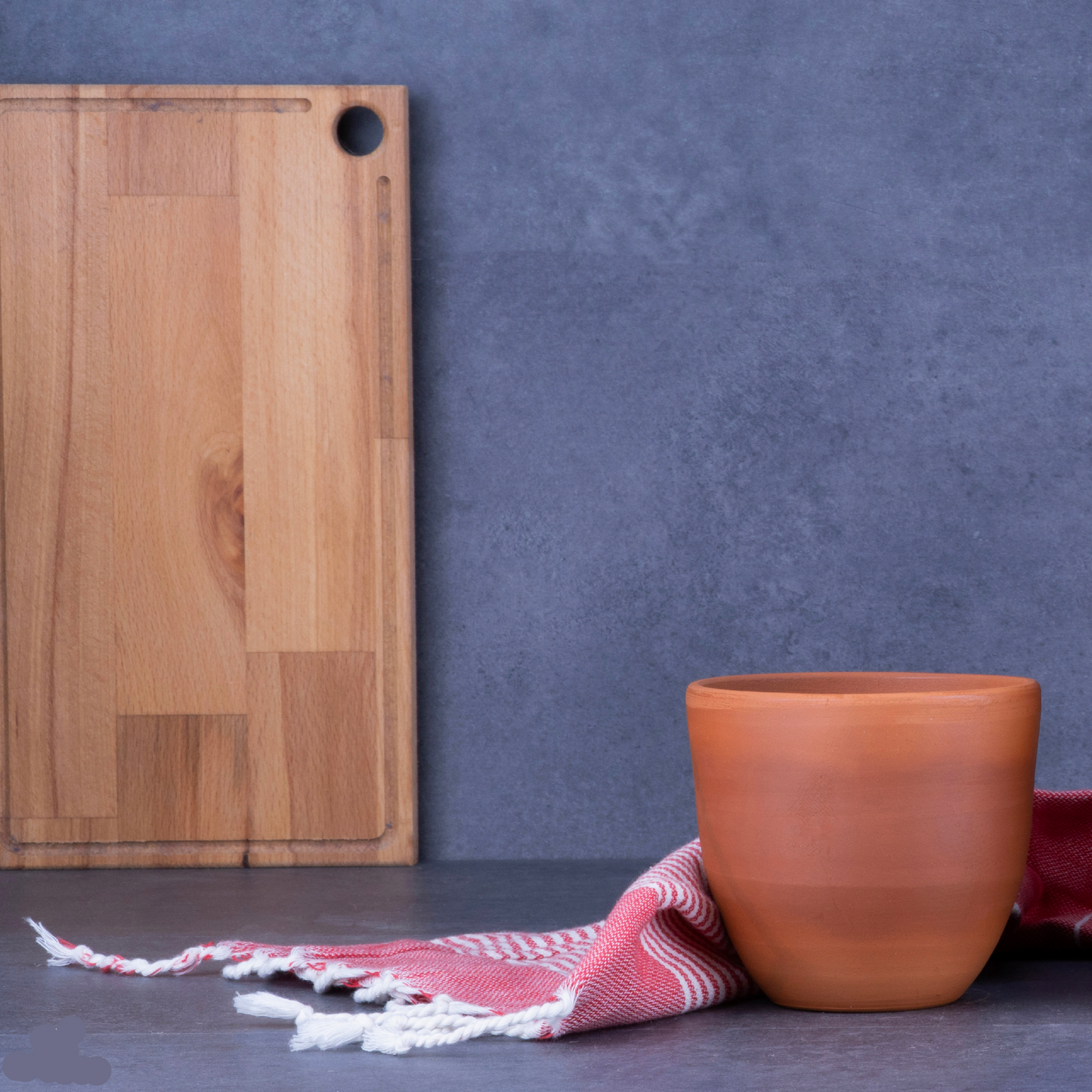 Wooden cutting board and terracotta pot on a dark surface with a blue background