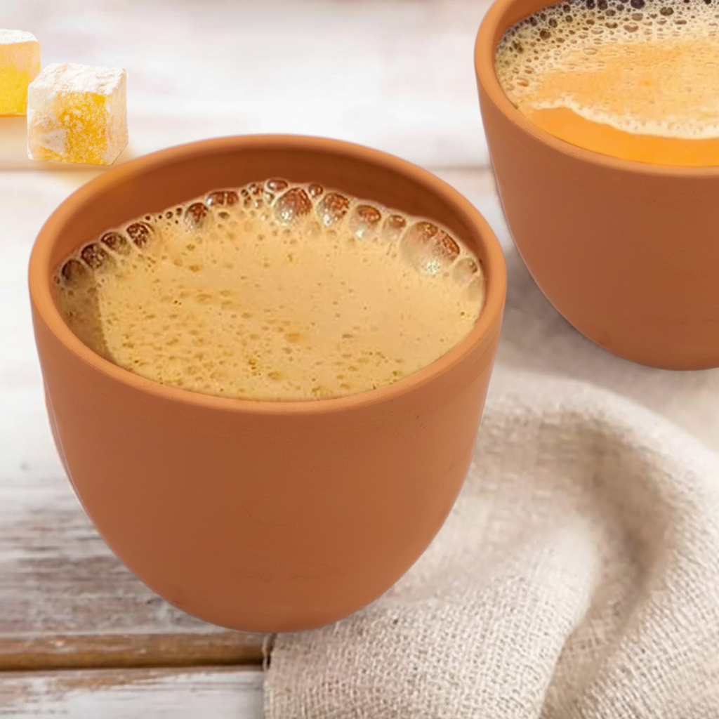 Two terracotta cups filled with a frothy beverage on a light wooden surface.